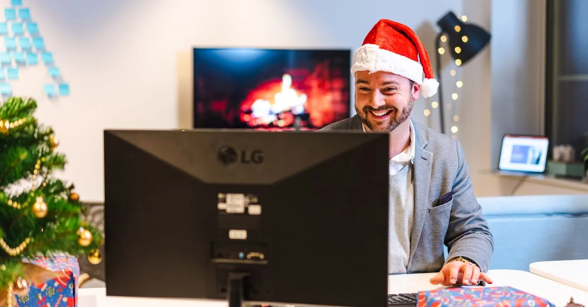 Homme d'affaires souriant portant un chapeau de Noël, travaillant à un bureau décoré pour Noël.