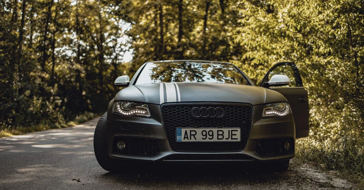 Vue de face d'une voiture Audi noire sur une route forestière avec une porte ouverte.