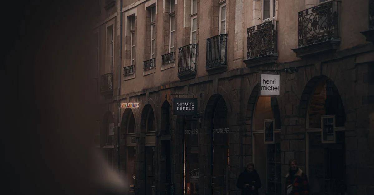 Une scène de rue faiblement éclairée représentant des façades de bâtiments européens classiques lors d'une soirée calme.