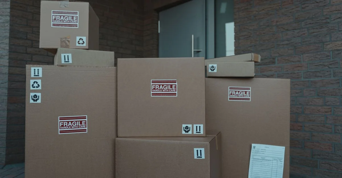 Plusieurs colis en carton marqués comme fragiles empilés à l'entrée d'un bâtiment.