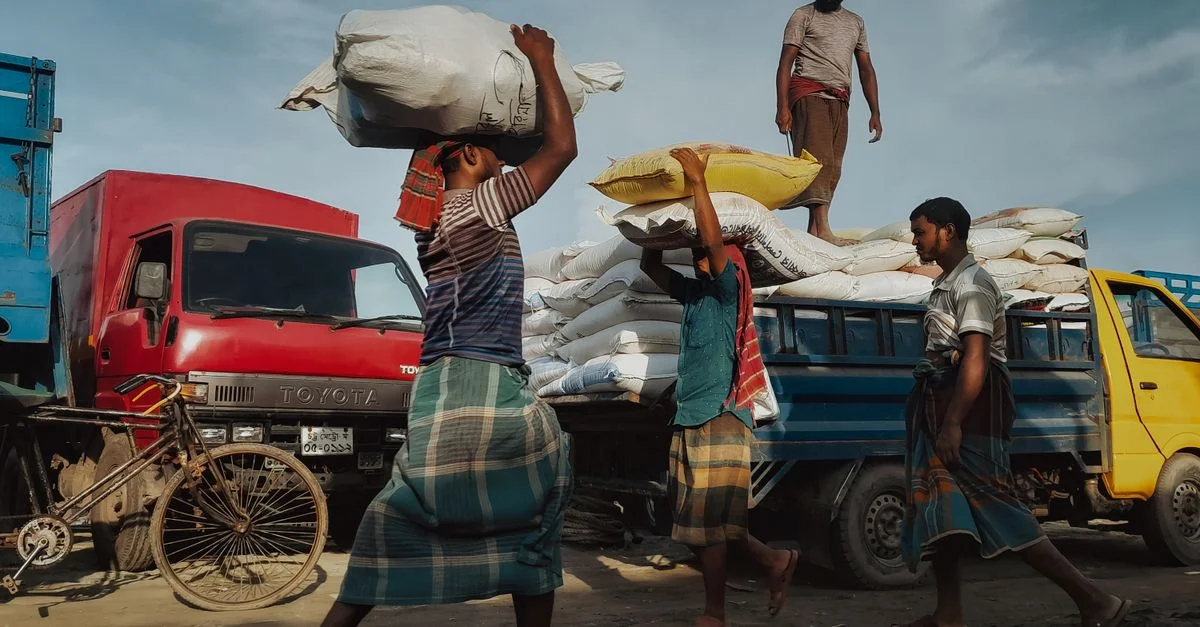 Des hommes chargent des sacs sur des camions à Chattogram, illustrant le travail d'équipe et la labeur dans un environnement animé.