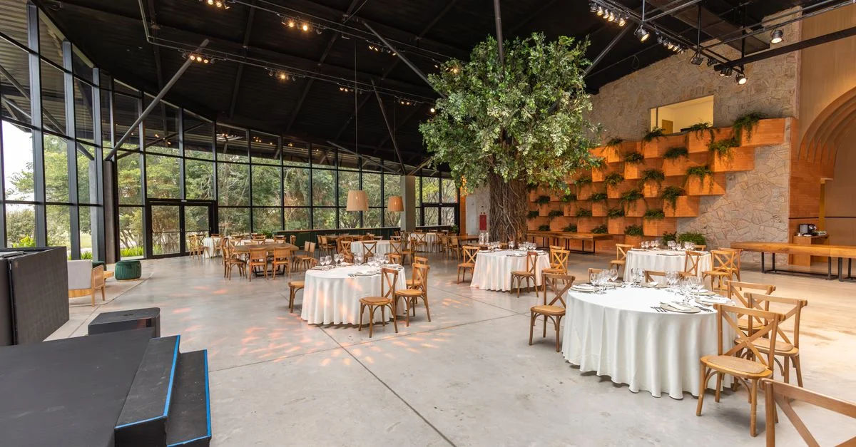 Une salle de banquet spacieuse avec une décoration moderne, une végétation luxuriante et un éclairage élégant préparée pour un événement.