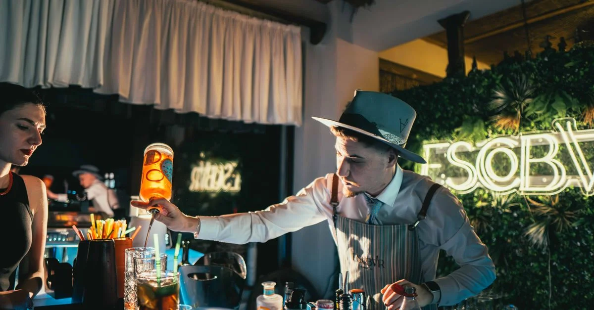 Barman mélangeant habilement un cocktail dans un bar tendance illuminé au néon avec une ambiance animée.