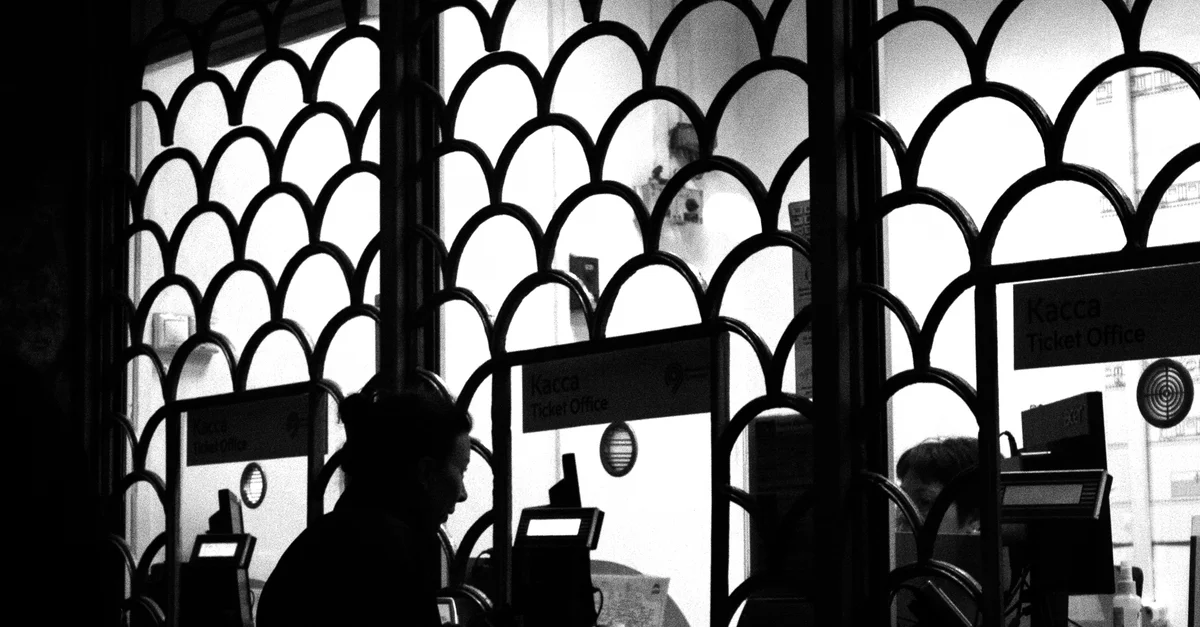 Femme en silhouette à la fenêtre d'un guichet, capturée en noir et blanc pour un effet dramatique.