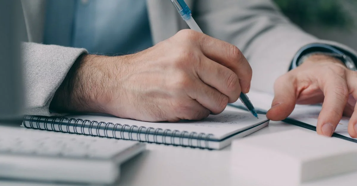 Gros plan d'un homme d'affaires prenant des notes dans un cahier à un bureau.