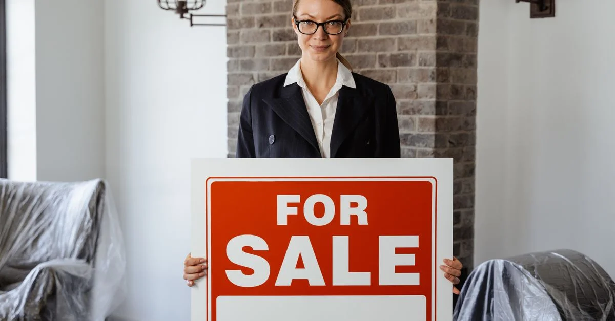 Agent immobilier professionnel tenant un panneau 'À vendre' dans un intérieur moderne.