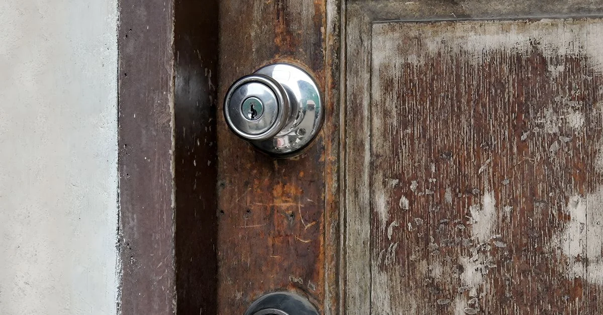 Gros plan d'une porte en bois patiné avec des serrures en métal, présentant des éléments vieillis et rustiques.