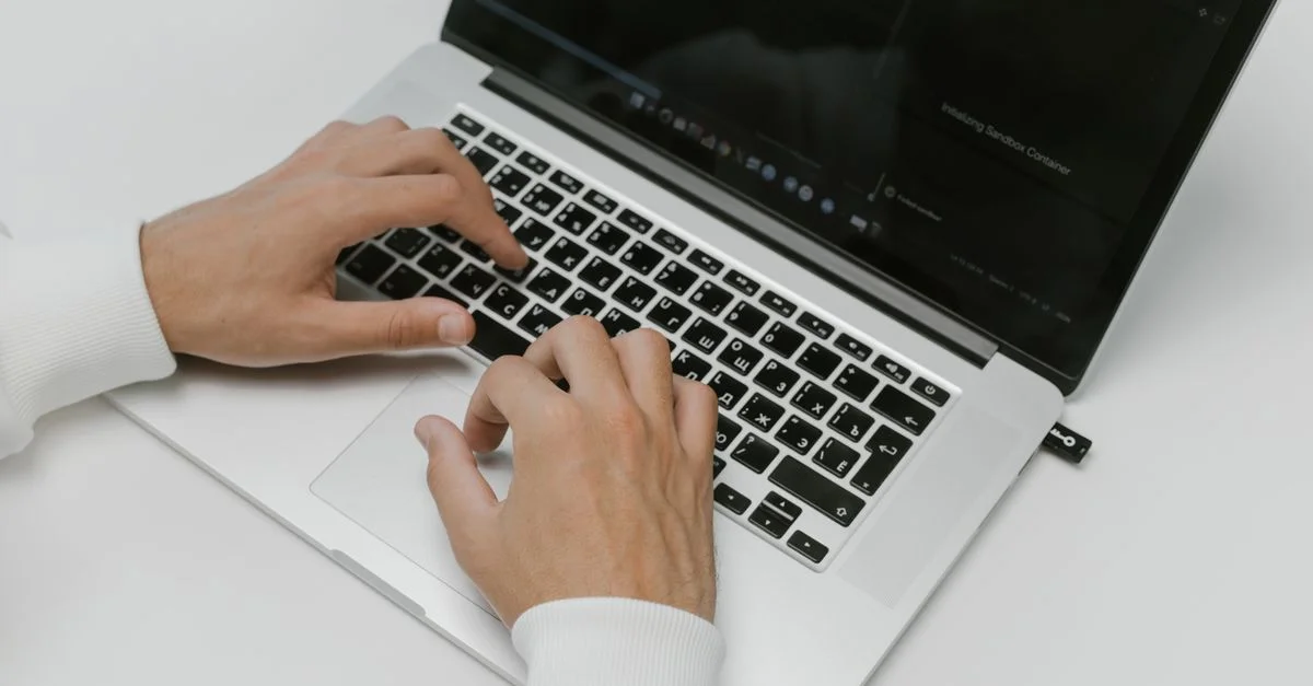 Gros plan sur des mains tapant sur un ordinateur portable avec un périphérique USB sur un fond blanc. Idéal pour des thèmes technologiques et de cybersécurité.