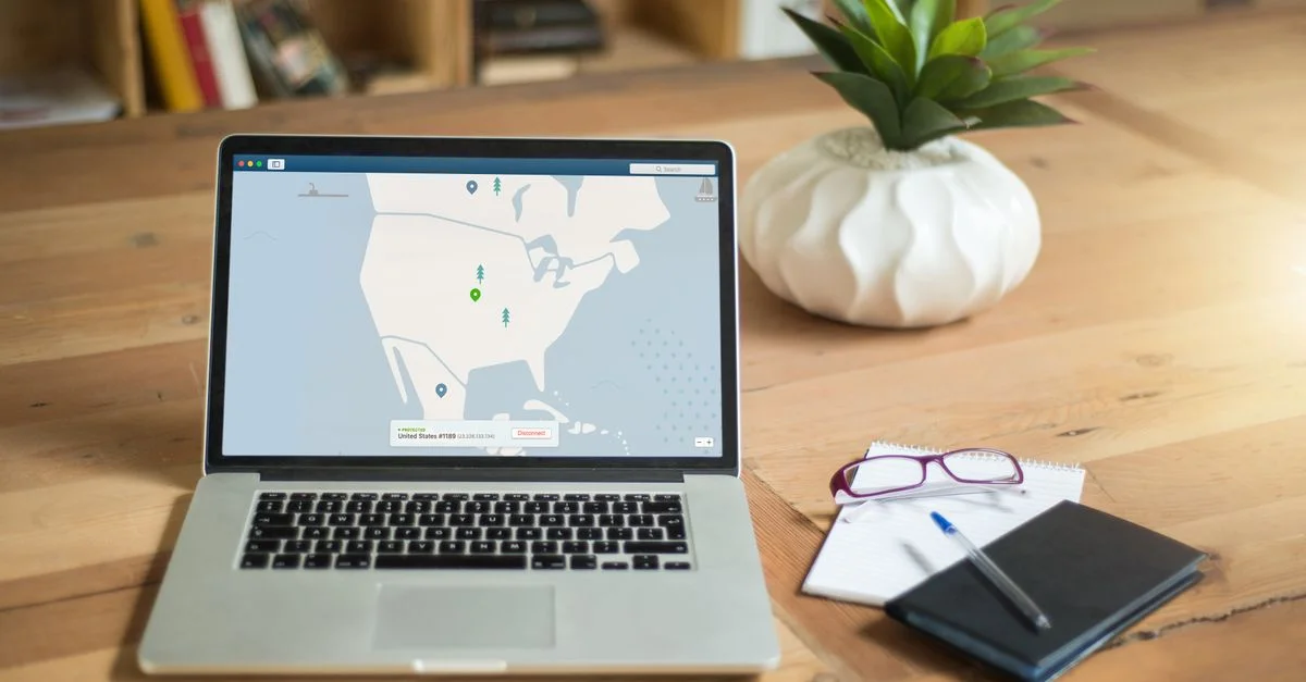 Un ordinateur portable affichant un logiciel VPN est posé sur un bureau en bois avec un bloc-notes et une plante, offrant une ambiance de travail sécurisé.