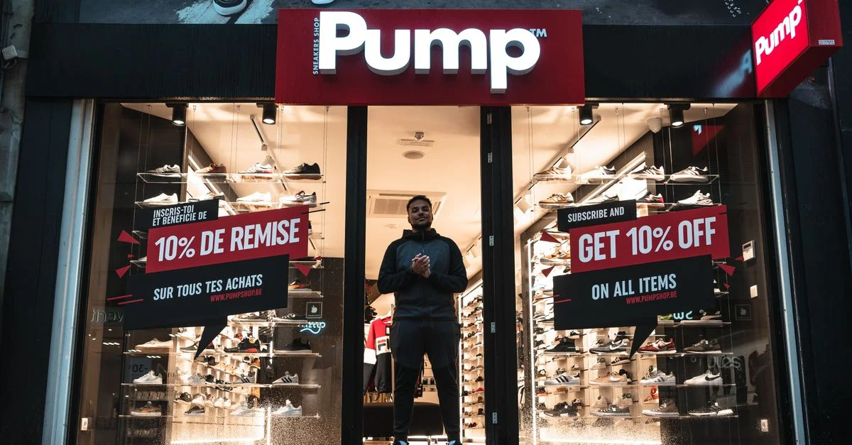 Magasin de chaussures Pump illuminé à Bruxelles avec des panneaux de soldes et des reflets la nuit.