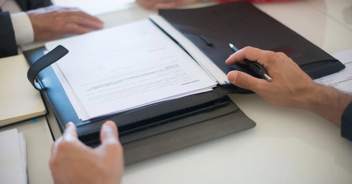 Deux professionnels discutent d'un contrat avec des documents sur une table, à l'intérieur.