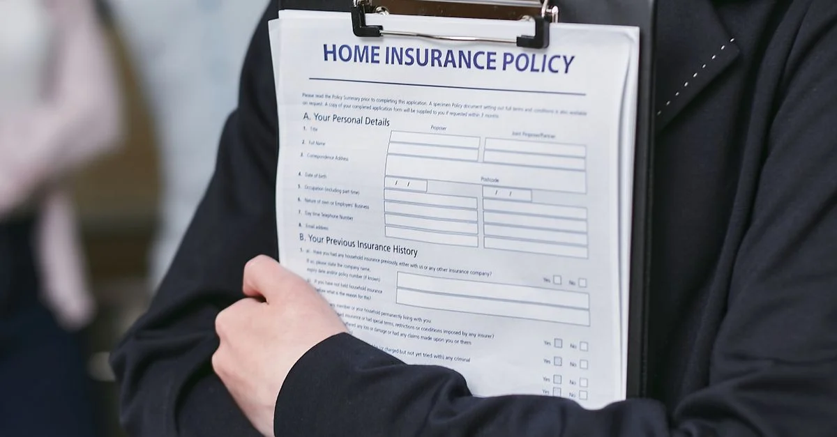 Gros plan sur une personne tenant une police d'assurance habitation sur un clipboard, capturé à l'intérieur.