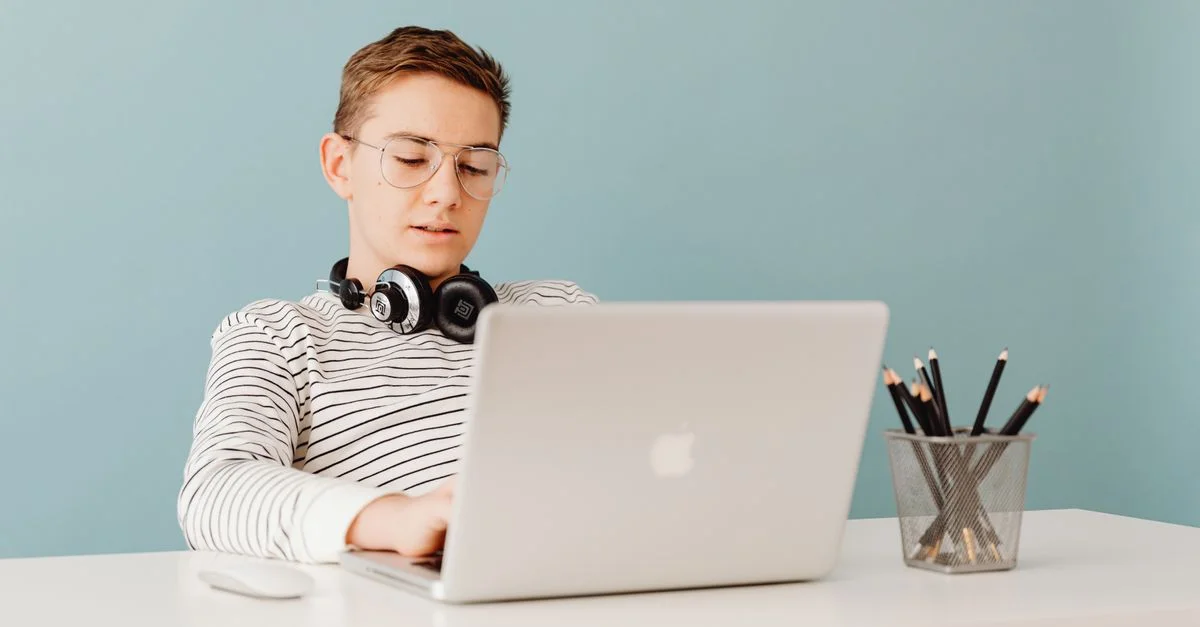 Adolescent masculin avec des écouteurs travaillant sur un ordinateur portable à une table, mettant en avant un accent sur la technologie.