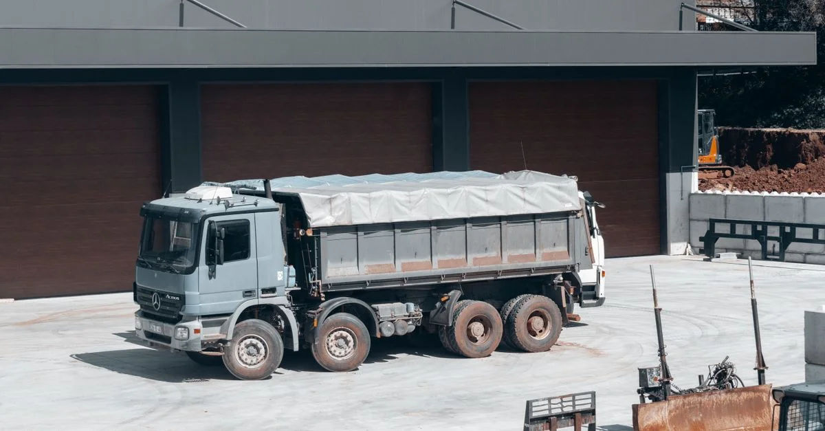 Un gros camion-benne stationné sur un chantier industriel près d'un bâtiment.