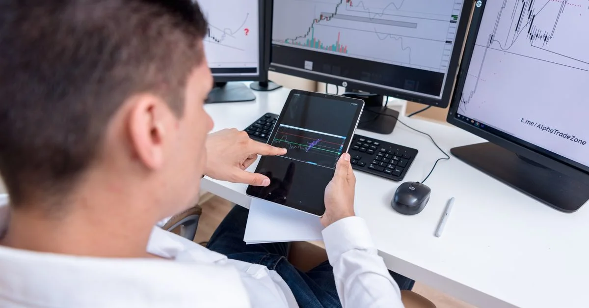 Un trader analysant des graphiques de cryptomonnaie sur plusieurs écrans et une tablette.