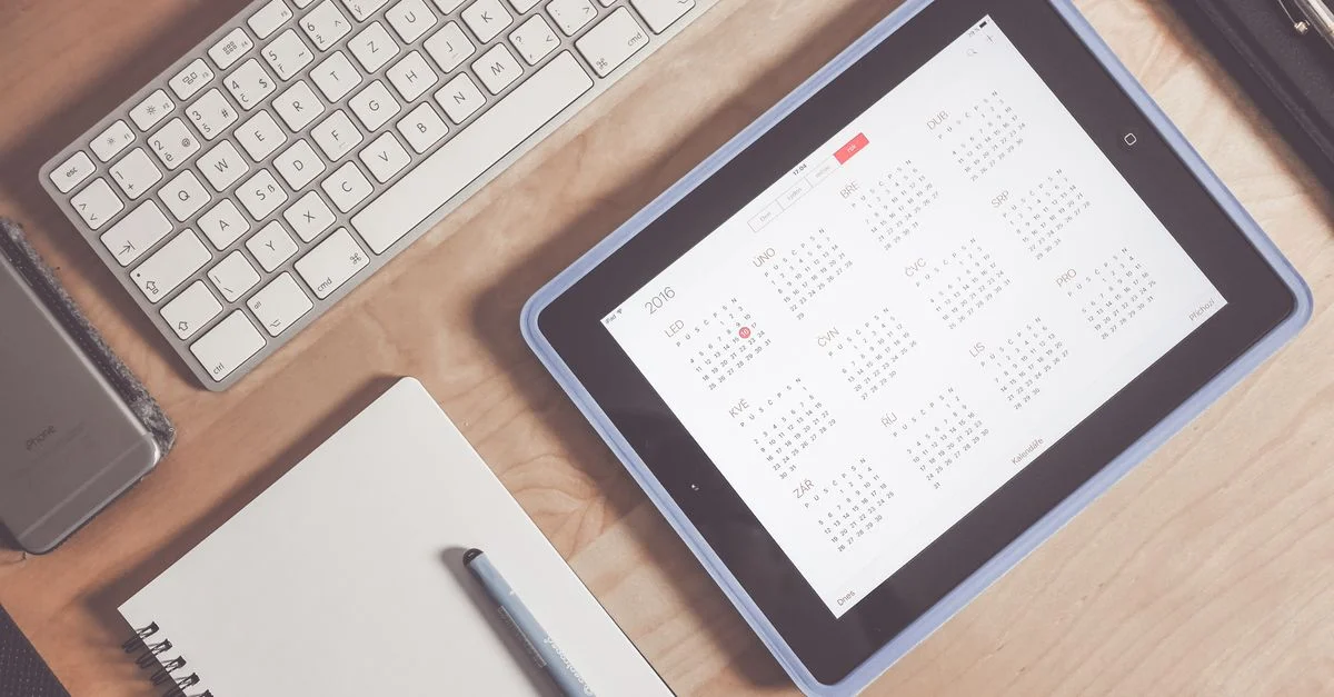 Un bureau bien rangé avec une tablette affichant un calendrier, un clavier et des fournitures de bureau.