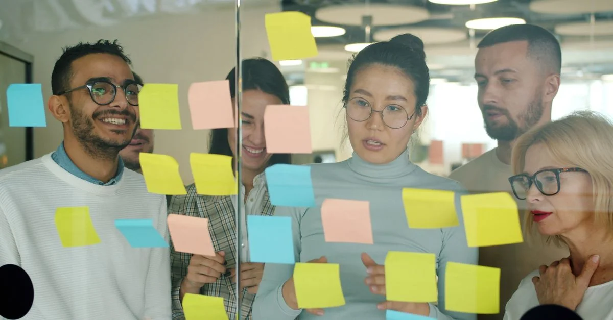 Une équipe aux profils variés élabore des stratégies à l'aide de post-it colorés sur une paroi vitrée du bureau.