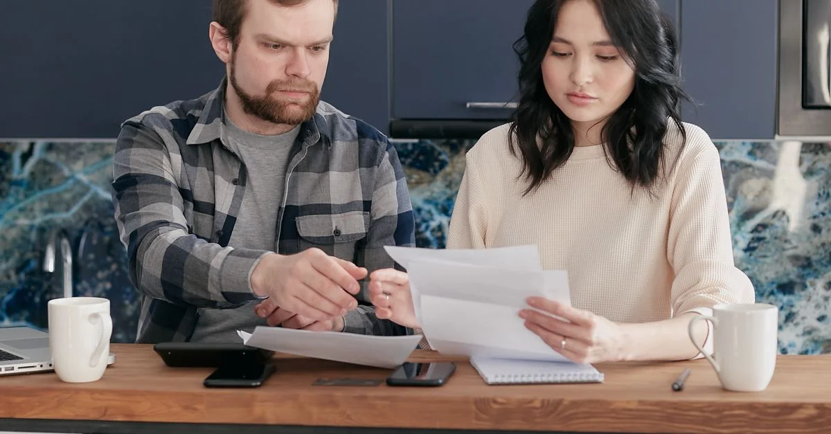 Un jeune couple examine des factures et un budget ensemble dans une cuisine moderne.