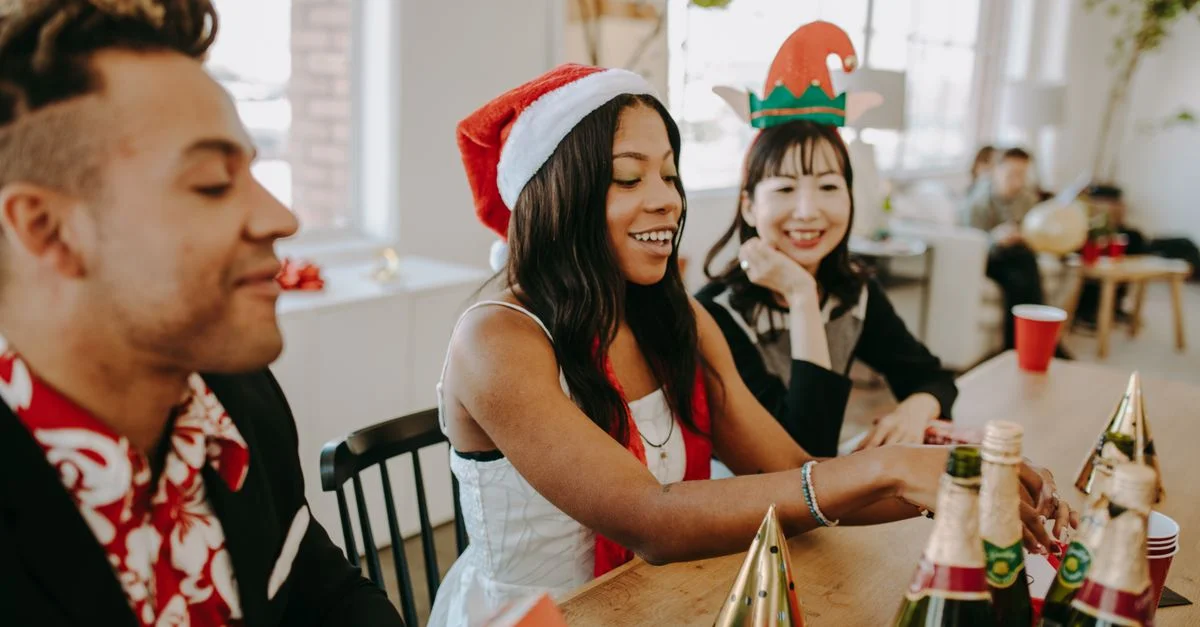 Des collègues divers profitant d'une joyeuse fête de Noël au bureau avec des boissons et des chapeaux festifs.