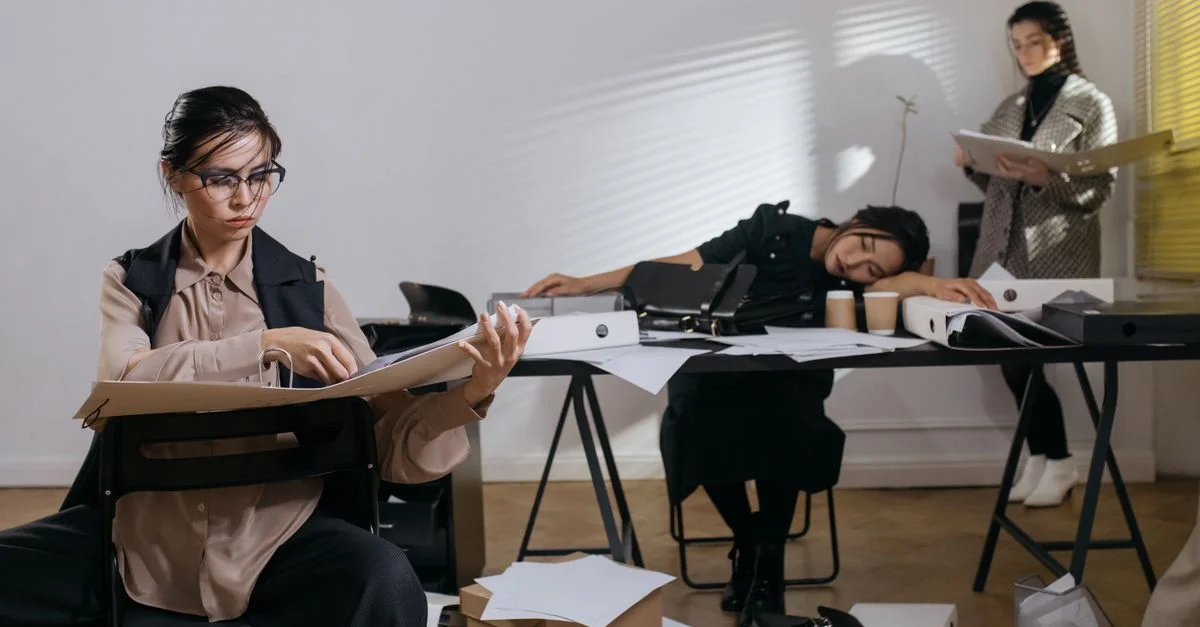 Trois femmes submergées par des paperasses dans un bureau en désordre.