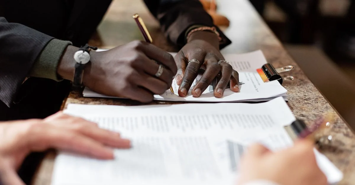 Gros plan sur des mains signant des documents dans un contexte professionnel, mettant en avant le professionnalisme et le travail d'équipe.
