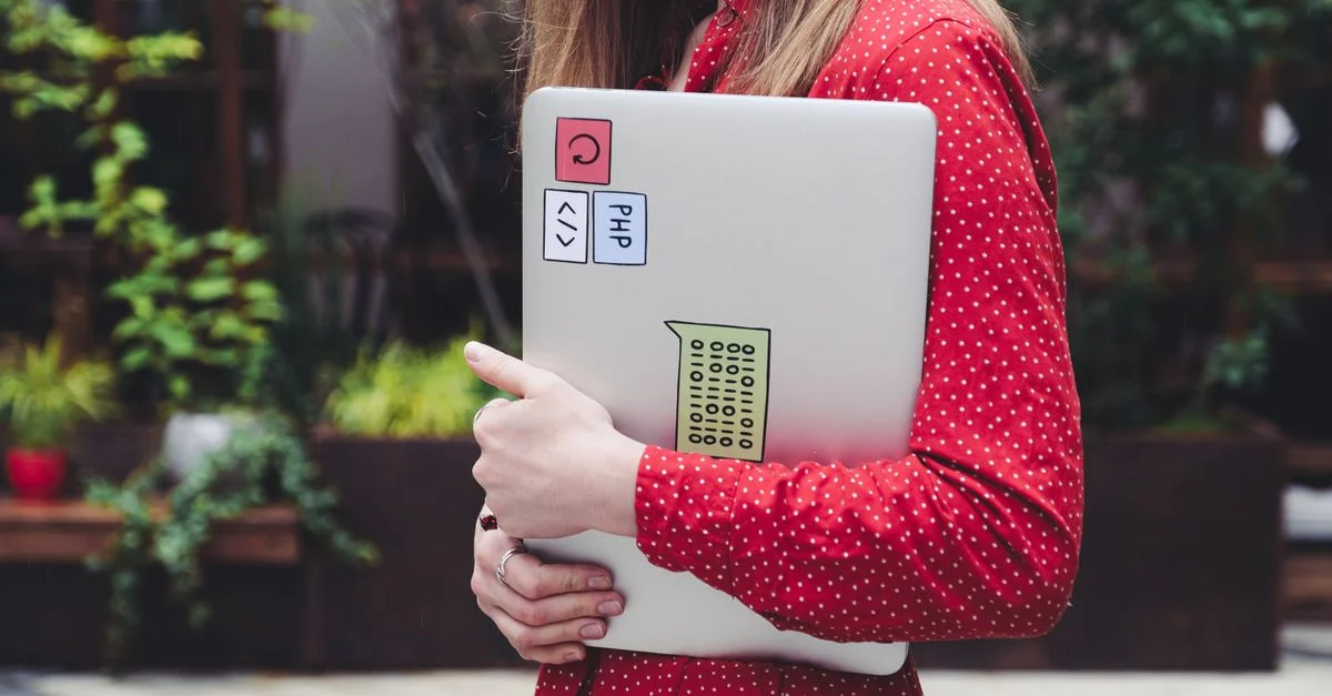 Une jeune femme portant une chemise à pois rouges tient un ordinateur portable avec des autocollants à l'extérieur.