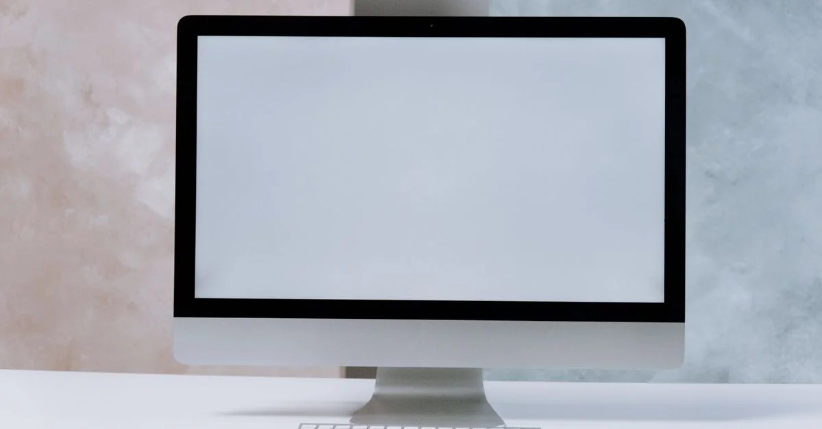 Un ordinateur de bureau iMac élégant sur un bureau blanc minimaliste avec un clavier et une souris.