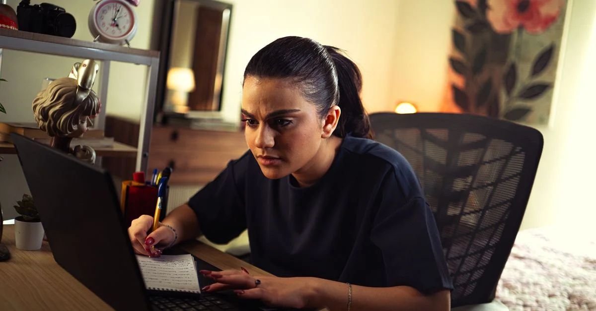Jeune femme étudiant intensément sur un ordinateur portable à un bureau bien éclairé à l'intérieur.