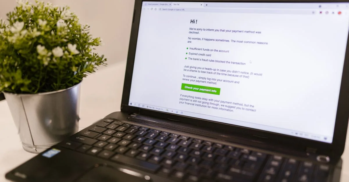 Ordinateur portable affichant un avis de refus de méthode de paiement à côté d'une plante en pot sur une surface blanche.