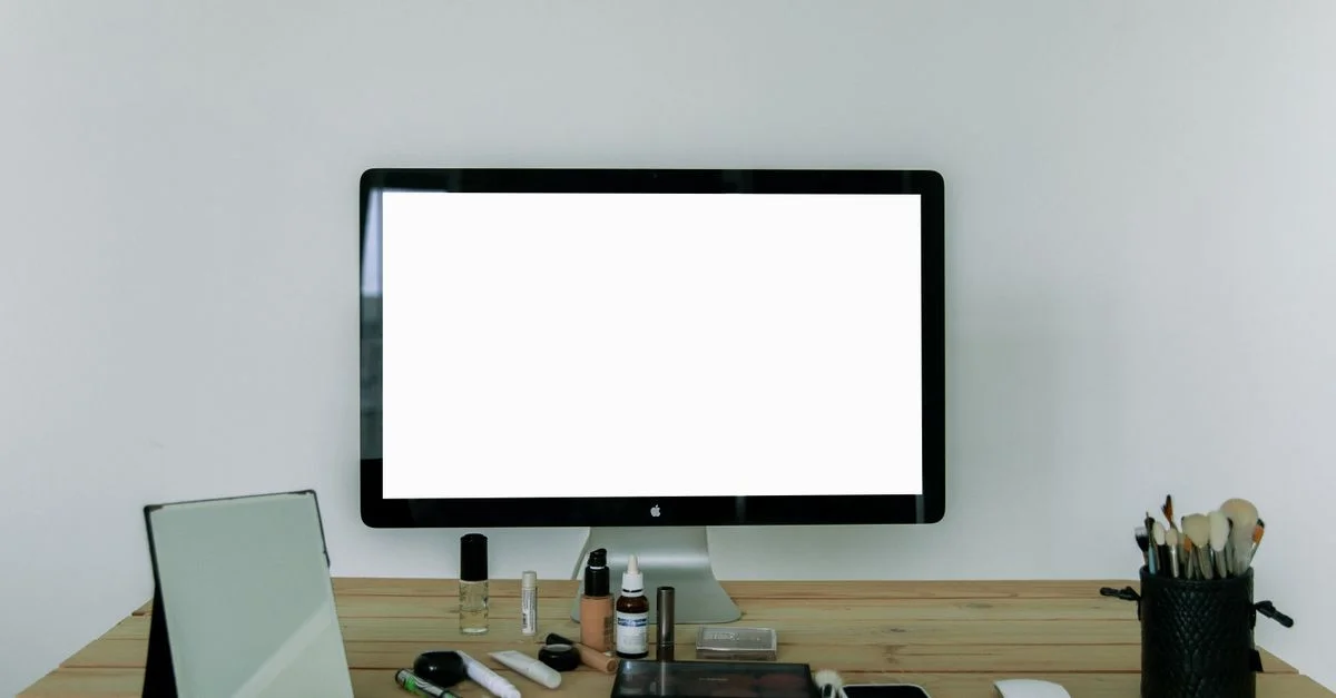 Un bureau soigneusement agencé avec un écran d'ordinateur, des outils de maquillage et un miroir, parfait pour les espaces de travail modernes.