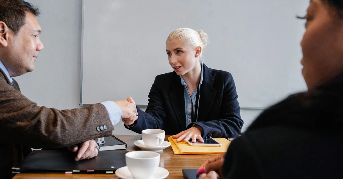 Trois professionnels en réunion échangeant une poignée de main autour d'un café, symbolisant accord et collaboration.
