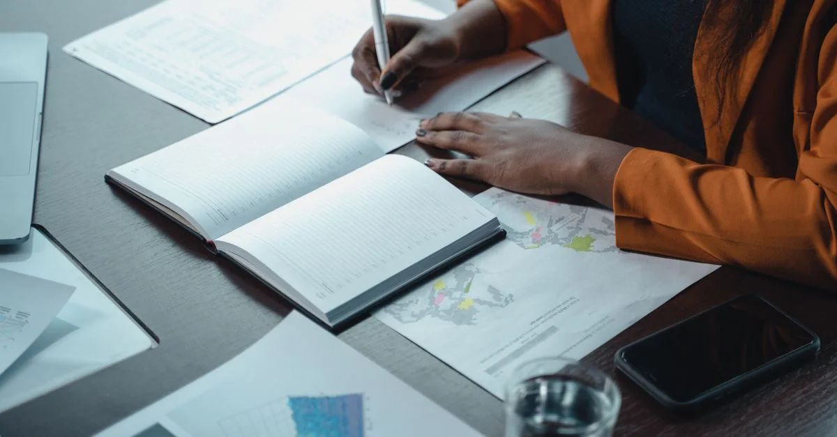 Une femme d'affaires écrit dans un carnet tout en examinant des graphiques et des courbes dans un cadre de bureau.