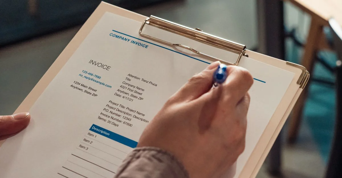 Main d'une personne tenant une facture d'entreprise sur un carnet avec un stylo.