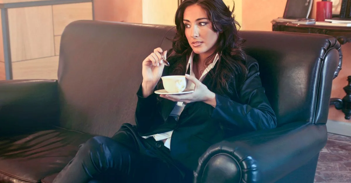 Femme d'affaires élégante profitant d'une pause café dans un salon de bureau moderne, exprimant relaxation et élégance.
