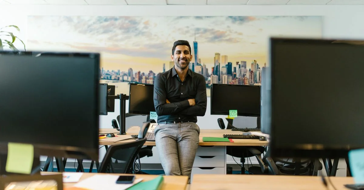Homme d'affaires professionnel souriant dans un environnement de bureau contemporain avec fond de paysage urbain.